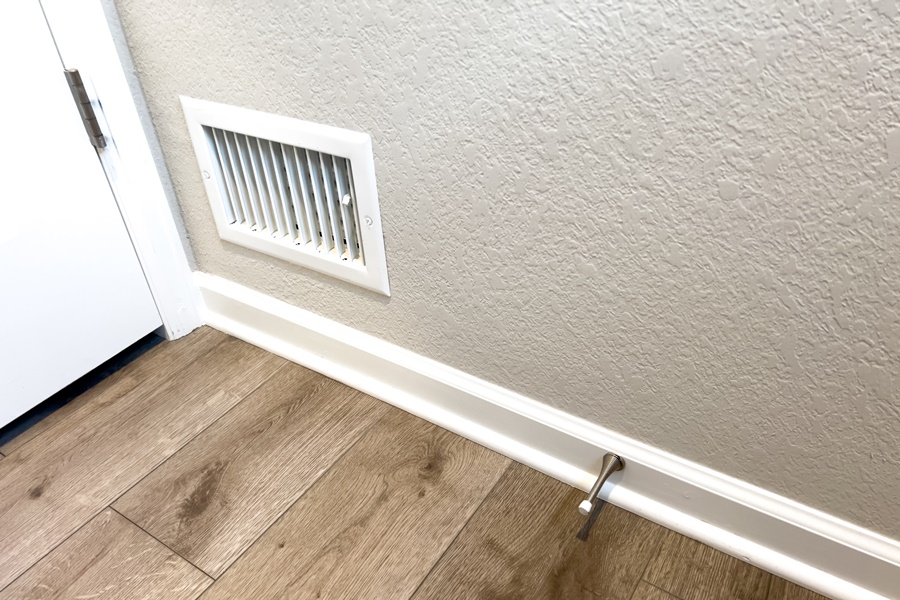 Rejilla de ventilación instalada abajo en pared interior, ideal para entrada de aire en sistemas de ventilación doméstica.