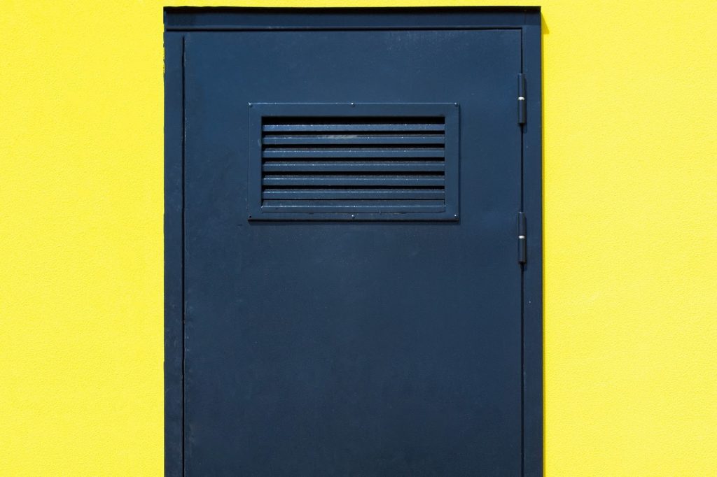 Puerta metálica azul con rejilla de ventilación rectangular, ideal para zonas técnicas donde las rejillas para puertas son necesarias por seguridad.