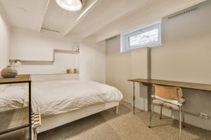 Dormitorio en un espacio subterráneo con ventana elevada y rejillas en pared, ejemplo de cómo puedo ventilar un espacio subterráneo habitado.