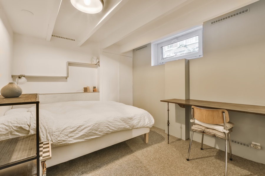 Dormitorio en un espacio subterráneo con ventana elevada y rejillas en pared, ejemplo de cómo puedo ventilar un espacio subterráneo habitado.