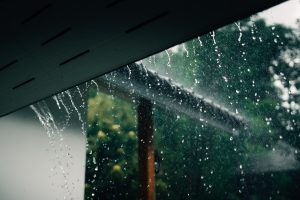 Vista exterior durante una intensa lluvia, mostrando cómo el agua se desliza por el borde del tejado, un entorno donde las rejillas de ventilación lluvia deben estar correctamente protegidas para evitar filtraciones.