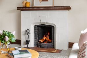 Chimenea encendida en salón con revestimiento blanco, ilustrando dónde colocar rejillas de ventilación chimenea para mejorar la circulación de aire.