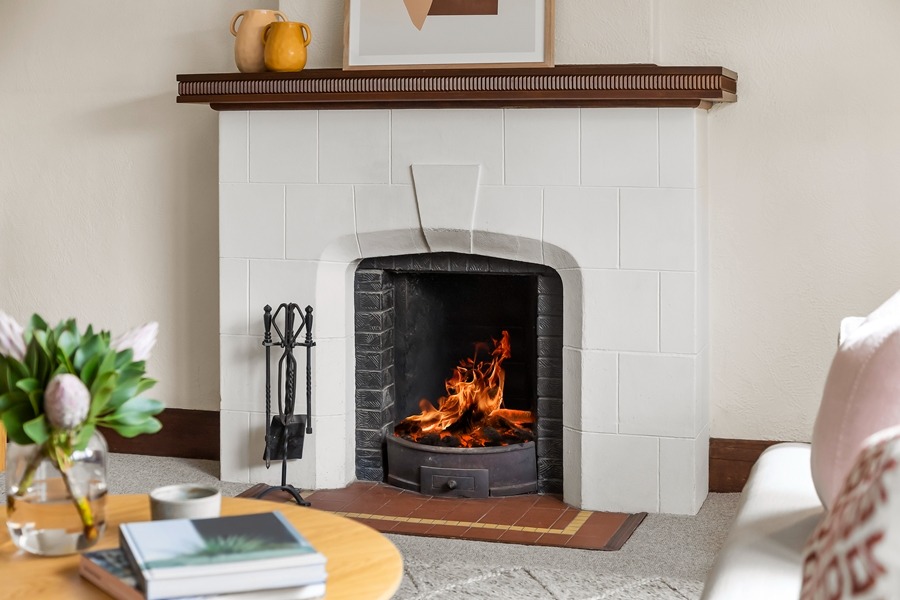 Chimenea encendida en salón con revestimiento blanco, ilustrando dónde colocar rejillas de ventilación chimenea para mejorar la circulación de aire.