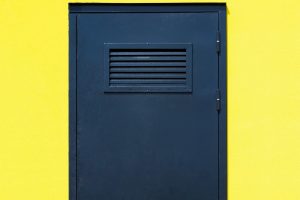 Puerta metálica azul con rejilla de ventilación rectangular, ideal para zonas técnicas donde las rejillas para puertas son necesarias por seguridad.