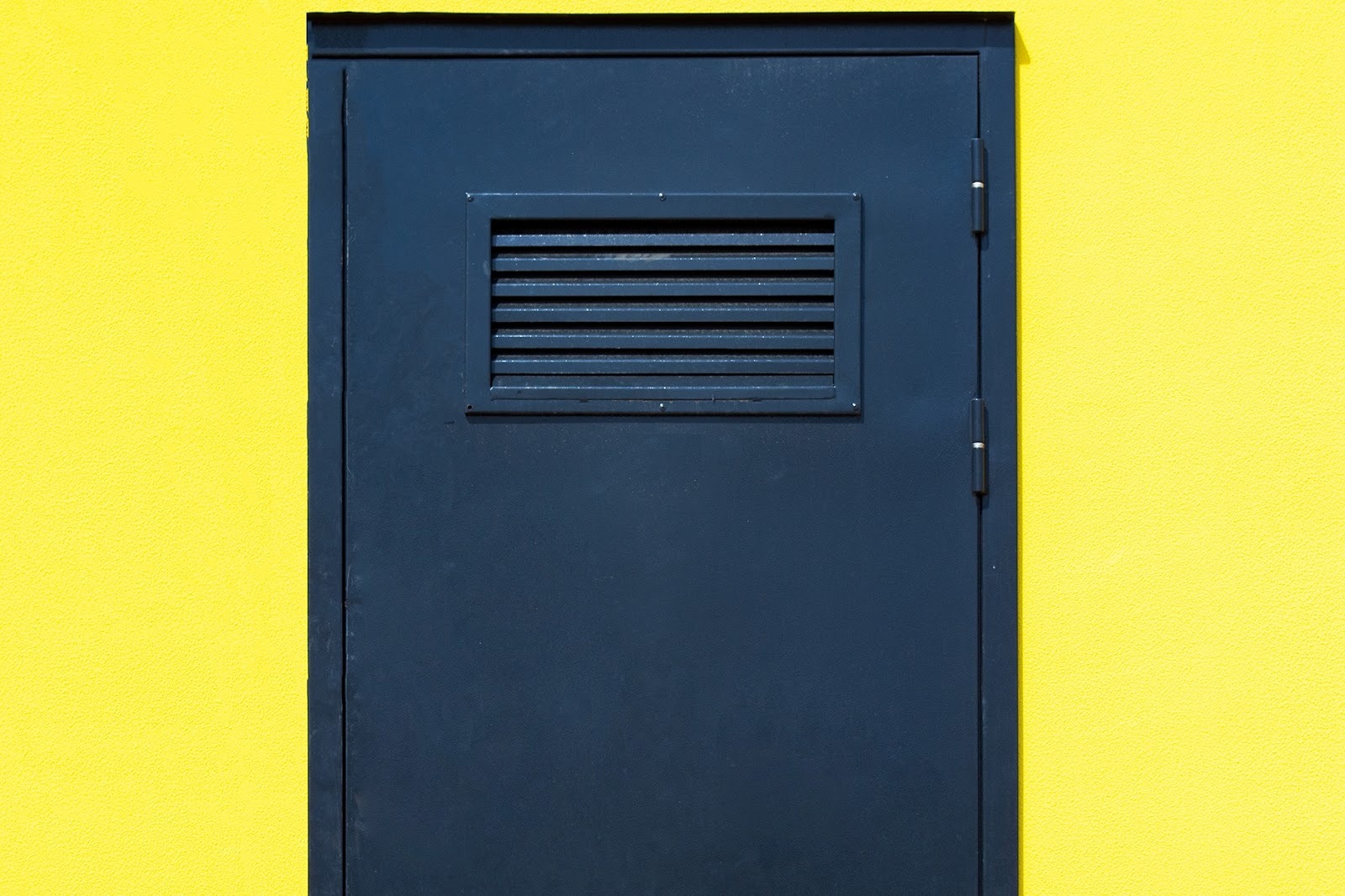 Puerta metálica azul con rejilla de ventilación rectangular, ideal para zonas técnicas donde las rejillas para puertas son necesarias por seguridad.